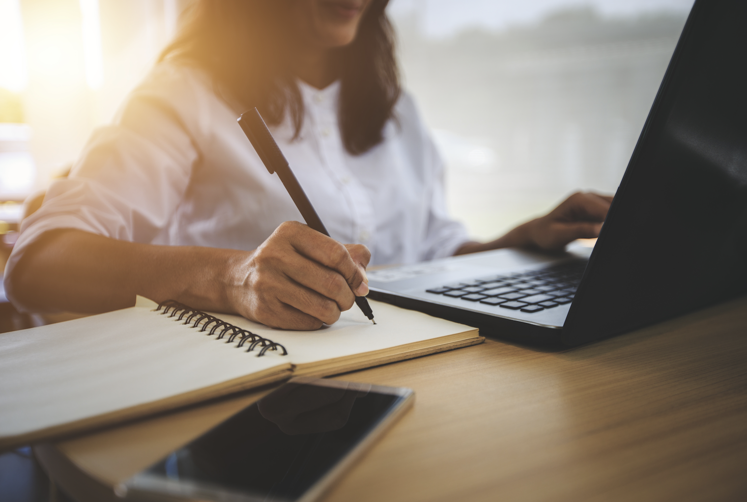 A woman writing at a desk alongside computer